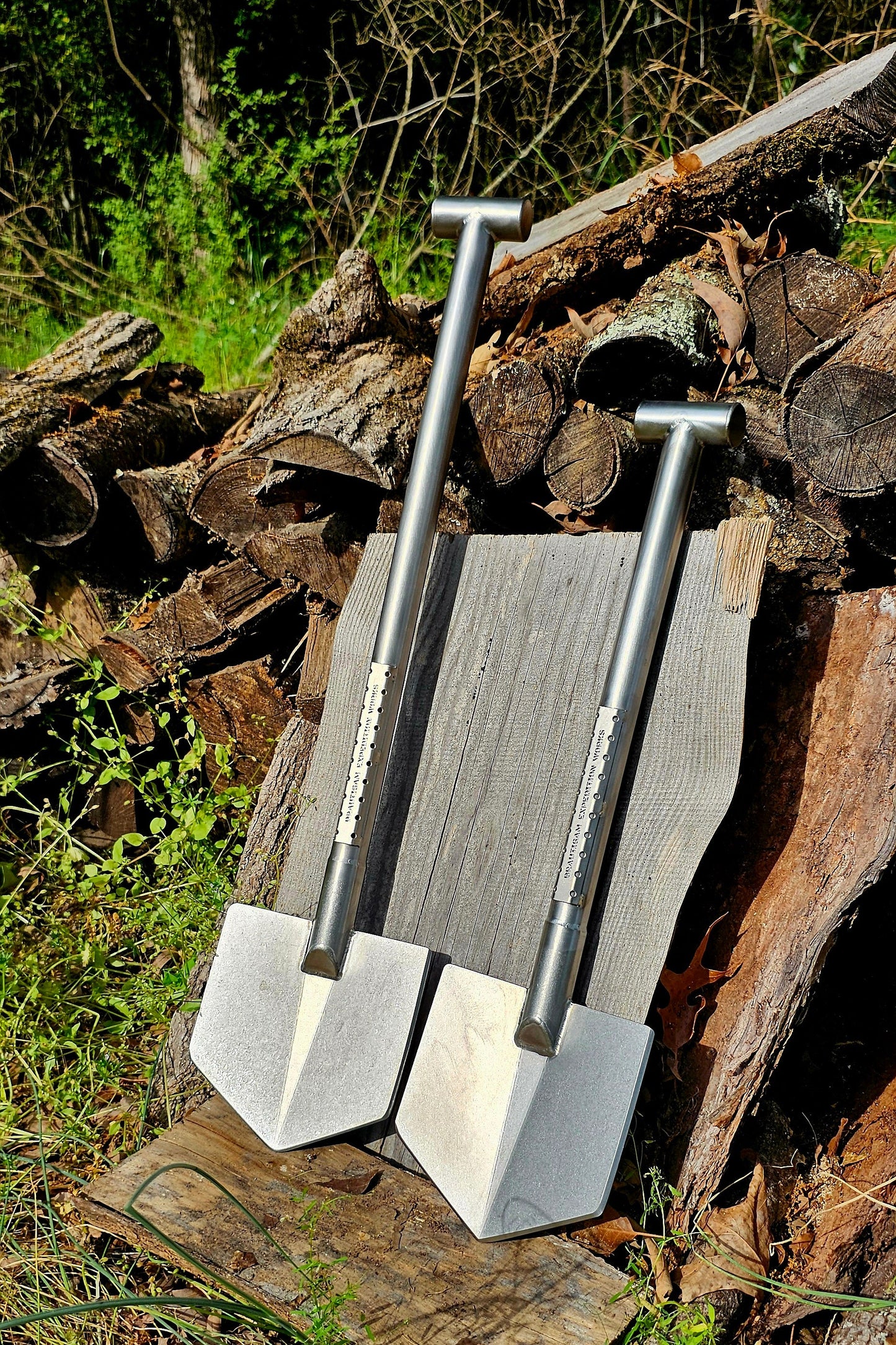 Two metal shovels leaning against a pile of wood with a natural outdoor background.
