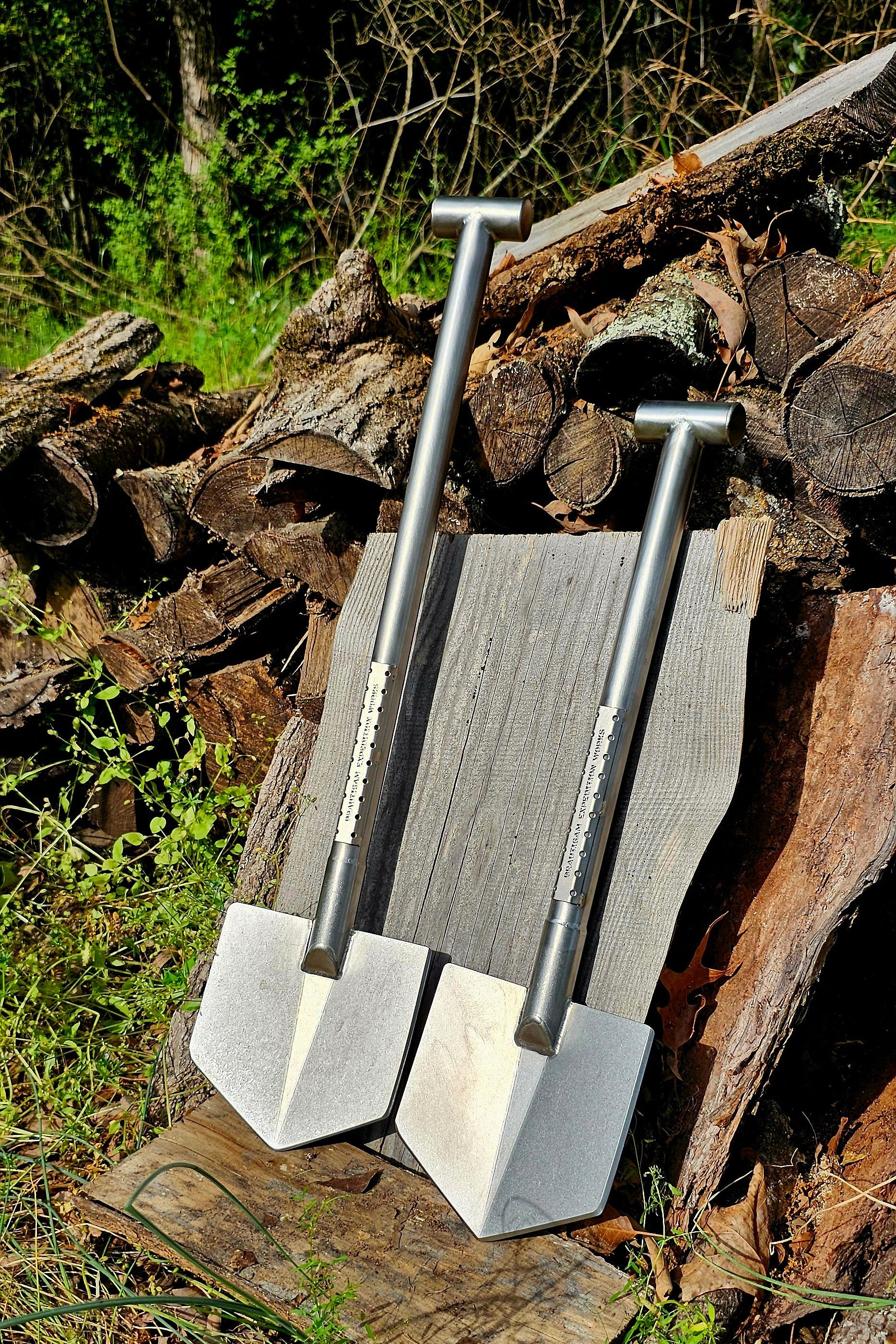 Two metal shovels leaning against a pile of wood with a natural outdoor background.