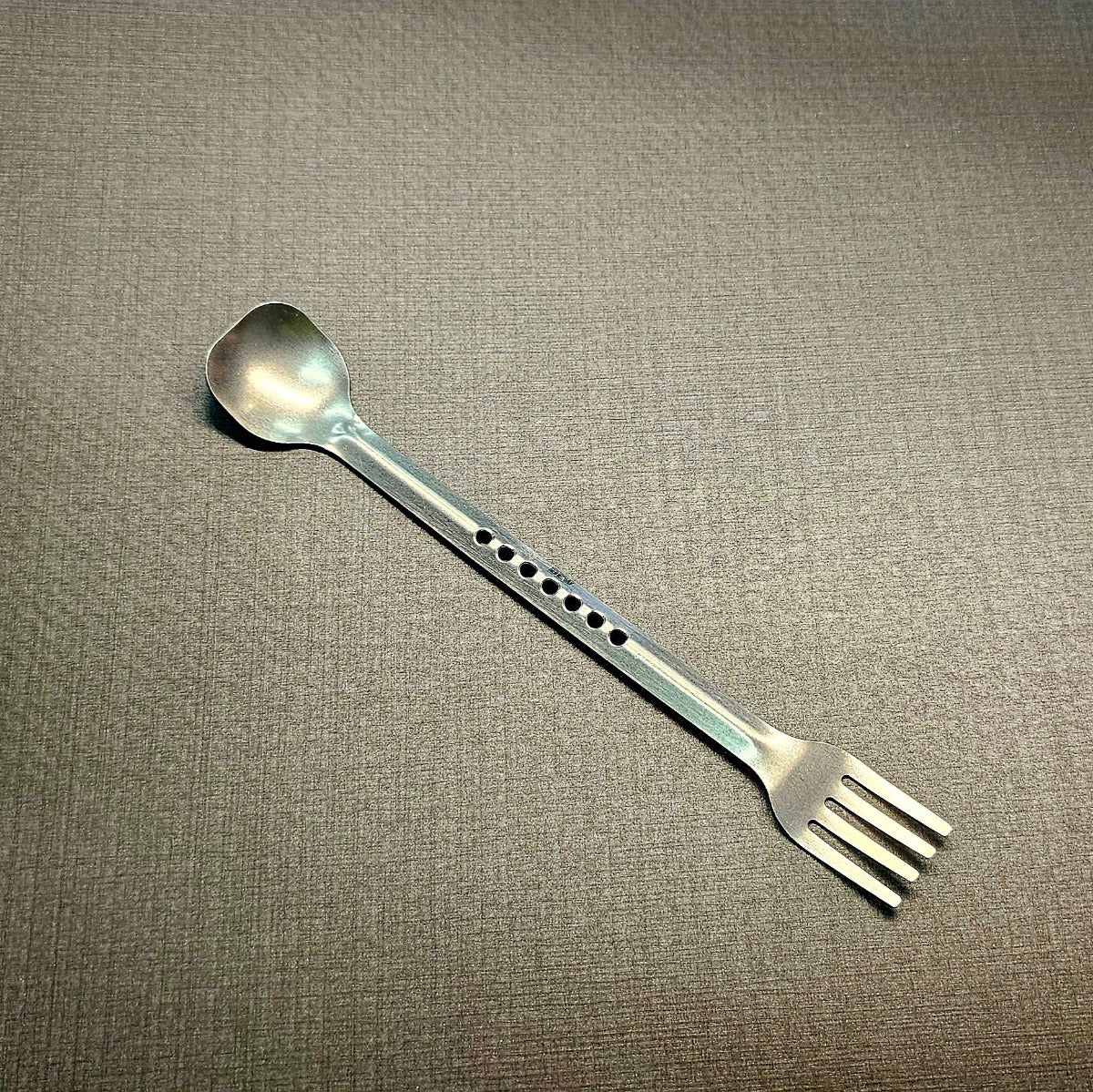 Metallic spoon and fork hybrid on a textured gray background